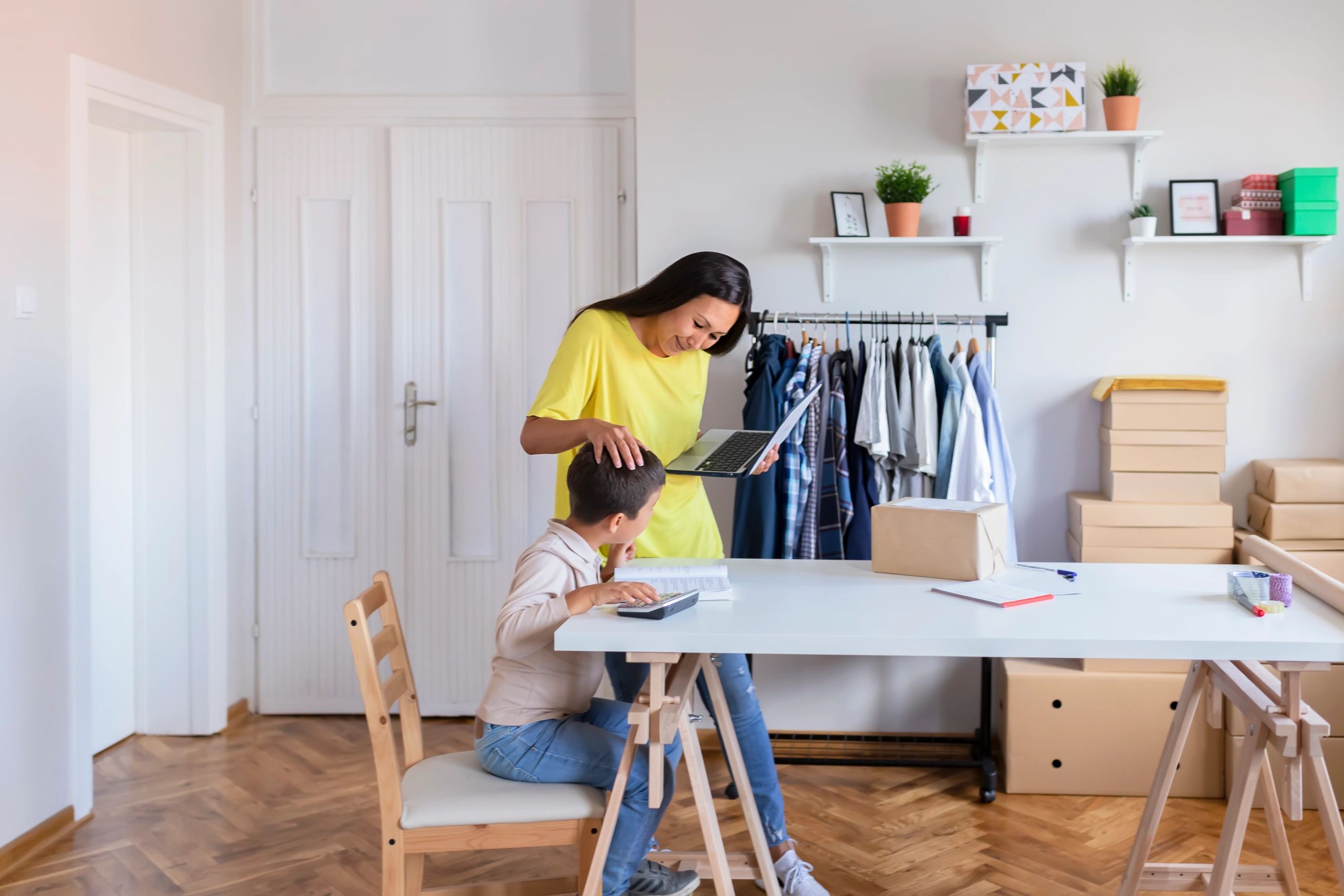 Mother working on a laptop while her child does homework nearby